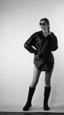 Siyah gömlekli ve güneş gözlüklü genç bir kadının stüdyoda poz verirken çekilmiş siyah beyaz bir fotoğrafı..  