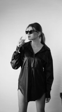 Siyah gömlekli ve güneş gözlüklü genç bir kadının stüdyoda poz verirken çekilmiş siyah beyaz bir fotoğrafı..  