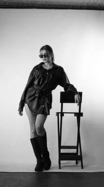 Siyah gömlekli ve güneş gözlüklü genç bir kadının stüdyoda poz verirken çekilmiş siyah beyaz bir fotoğrafı..  