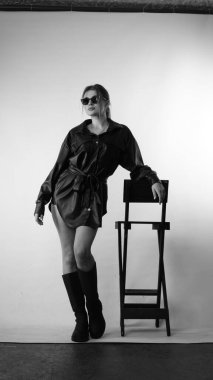 Siyah gömlekli ve güneş gözlüklü genç bir kadının stüdyoda poz verirken çekilmiş siyah beyaz bir fotoğrafı..  