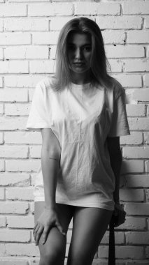 Uzun saçlı, uzun tişörtlü, stüdyoda sandalyeyle poz veren güzel bir kadının siyah beyaz fotoğrafı..  