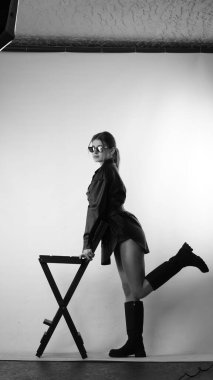 Siyah gömlekli ve güneş gözlüklü genç bir kadının stüdyoda poz verirken çekilmiş siyah beyaz bir fotoğrafı..  