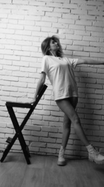 Stüdyoda sandalyenin yanında uzun saçlı, siyah beyaz bir kadın poz veriyor..  