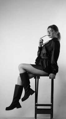 Siyah gömlekli ve güneş gözlüklü genç bir kadının stüdyoda poz verirken çekilmiş siyah beyaz bir fotoğrafı..  