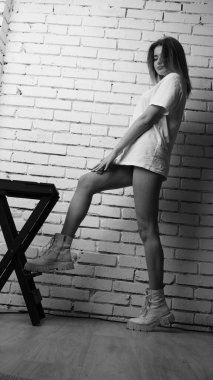 Stüdyoda sandalyenin yanında uzun saçlı, siyah beyaz bir kadın poz veriyor..  