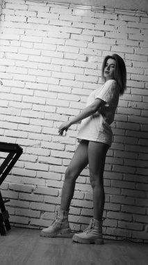 Stüdyoda sandalyenin yanında uzun saçlı, siyah beyaz bir kadın poz veriyor..  