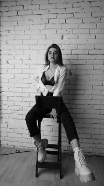 Beyaz tişörtlü, siyah beyaz saçlı, güzel ve seksi bir kadının stüdyoda beyaz bir duvara poz verdiği siyah beyaz bir fotoğraf..  