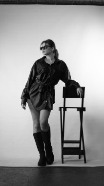 Siyah gömlekli ve güneş gözlüklü genç bir kadının stüdyoda poz verirken çekilmiş siyah beyaz bir fotoğrafı..  