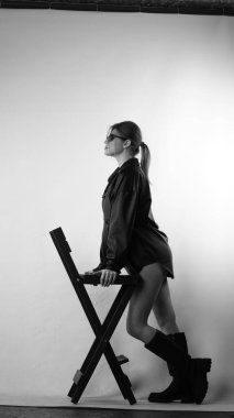 Siyah gömlekli ve güneş gözlüklü genç bir kadının stüdyoda poz verirken çekilmiş siyah beyaz bir fotoğrafı..  