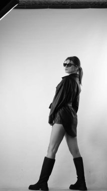 Siyah gömlekli ve güneş gözlüklü genç bir kadının stüdyoda poz verirken çekilmiş siyah beyaz bir fotoğrafı..  