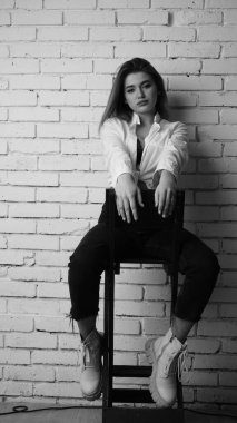 Beyaz tişörtlü, siyah beyaz saçlı, güzel ve seksi bir kadının stüdyoda beyaz bir duvara poz verdiği siyah beyaz bir fotoğraf..  