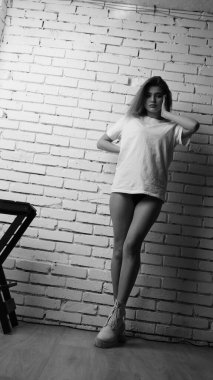 Stüdyoda sandalyenin yanında uzun saçlı, siyah beyaz bir kadın poz veriyor..  