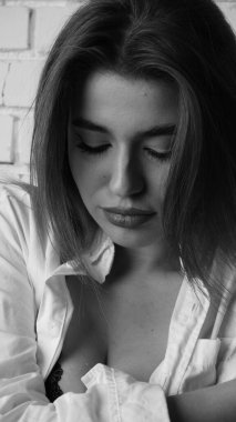 Beyaz tişörtlü, siyah beyaz saçlı, güzel ve seksi bir kadının stüdyoda beyaz bir duvara poz verdiği siyah beyaz bir fotoğraf..  