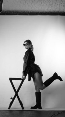 Siyah gömlekli ve güneş gözlüklü genç bir kadının stüdyoda poz verirken çekilmiş siyah beyaz bir fotoğrafı..  