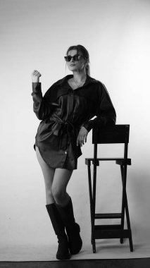 Siyah gömlekli ve güneş gözlüklü genç bir kadının stüdyoda poz verirken çekilmiş siyah beyaz bir fotoğrafı..  