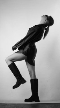 Siyah gömlekli ve güneş gözlüklü genç bir kadının stüdyoda poz verirken çekilmiş siyah beyaz bir fotoğrafı..  