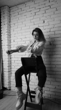 Beyaz tişörtlü, siyah beyaz saçlı, güzel ve seksi bir kadının stüdyoda beyaz bir duvara poz verdiği siyah beyaz bir fotoğraf..  