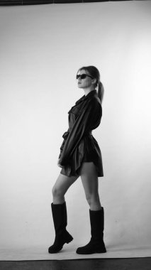 Siyah gömlekli ve güneş gözlüklü genç bir kadının stüdyoda poz verirken çekilmiş siyah beyaz bir fotoğrafı..  