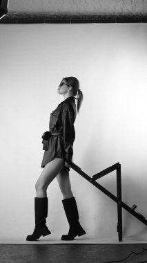 Siyah gömlekli ve güneş gözlüklü genç bir kadının stüdyoda poz verirken çekilmiş siyah beyaz bir fotoğrafı..  