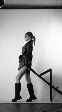 Siyah gömlekli ve güneş gözlüklü genç bir kadının stüdyoda poz verirken çekilmiş siyah beyaz bir fotoğrafı..  