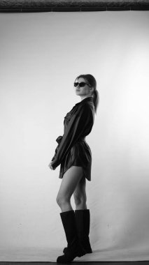 Siyah gömlekli ve güneş gözlüklü genç bir kadının stüdyoda poz verirken çekilmiş siyah beyaz bir fotoğrafı..  