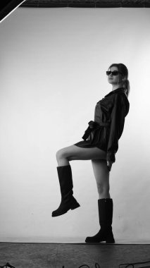 Siyah gömlekli ve güneş gözlüklü genç bir kadının stüdyoda poz verirken çekilmiş siyah beyaz bir fotoğrafı..  