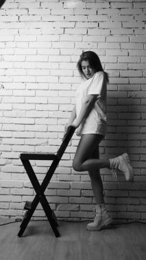 Stüdyoda sandalyenin yanında uzun saçlı, siyah beyaz bir kadın poz veriyor..  