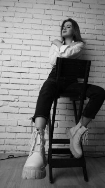 Beyaz tişörtlü, siyah beyaz saçlı, güzel ve seksi bir kadının stüdyoda beyaz bir duvara poz verdiği siyah beyaz bir fotoğraf..  