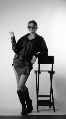 Siyah gömlekli ve güneş gözlüklü genç bir kadının stüdyoda poz verirken çekilmiş siyah beyaz bir fotoğrafı..  