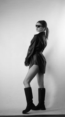 Siyah gömlekli ve güneş gözlüklü genç bir kadının stüdyoda poz verirken çekilmiş siyah beyaz bir fotoğrafı..  