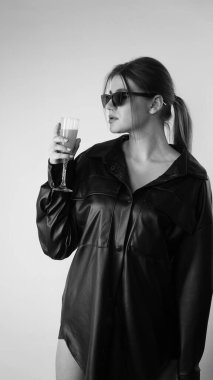 Siyah gömlekli ve güneş gözlüklü genç bir kadının stüdyoda poz verirken çekilmiş siyah beyaz bir fotoğrafı..  