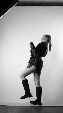 Siyah gömlekli ve güneş gözlüklü genç bir kadının stüdyoda poz verirken çekilmiş siyah beyaz bir fotoğrafı..  