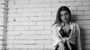 Beyaz tişörtlü, siyah beyaz saçlı, güzel ve seksi bir kadının stüdyoda beyaz bir duvara poz verdiği siyah beyaz bir fotoğraf..  