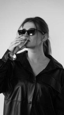 Siyah gömlekli ve güneş gözlüklü genç bir kadının stüdyoda poz verirken çekilmiş siyah beyaz bir fotoğrafı..  