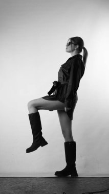 Siyah gömlekli ve güneş gözlüklü genç bir kadının stüdyoda poz verirken çekilmiş siyah beyaz bir fotoğrafı..  