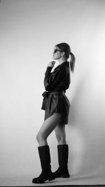 Siyah gömlekli ve güneş gözlüklü genç bir kadının stüdyoda poz verirken çekilmiş siyah beyaz bir fotoğrafı..  