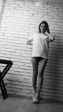 Stüdyoda sandalyenin yanında uzun saçlı, siyah beyaz bir kadın poz veriyor..  