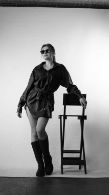 Siyah gömlekli ve güneş gözlüklü genç bir kadının stüdyoda poz verirken çekilmiş siyah beyaz bir fotoğrafı..  