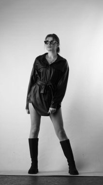 Siyah gömlekli ve güneş gözlüklü genç bir kadının stüdyoda poz verirken çekilmiş siyah beyaz bir fotoğrafı..  