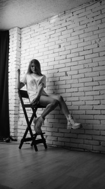 Stüdyoda sandalyenin yanında uzun saçlı, siyah beyaz bir kadın poz veriyor..  