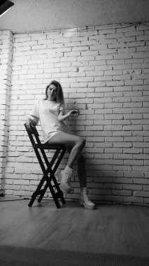 Stüdyoda sandalyenin yanında uzun saçlı, siyah beyaz bir kadın poz veriyor..  