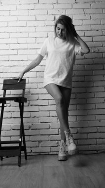 Stüdyoda sandalyenin yanında uzun saçlı, siyah beyaz bir kadın poz veriyor..  