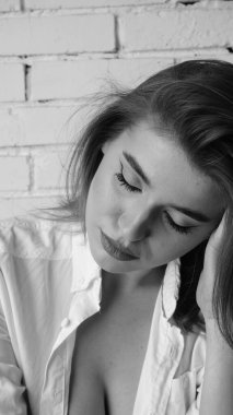 Beyaz tişörtlü, siyah beyaz saçlı, güzel ve seksi bir kadının stüdyoda beyaz bir duvara poz verdiği siyah beyaz bir fotoğraf..  