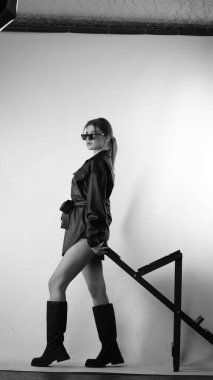 Siyah gömlekli ve güneş gözlüklü genç bir kadının stüdyoda poz verirken çekilmiş siyah beyaz bir fotoğrafı..  