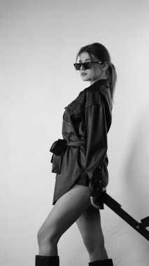 Siyah gömlekli ve güneş gözlüklü genç bir kadının stüdyoda poz verirken çekilmiş siyah beyaz bir fotoğrafı..  