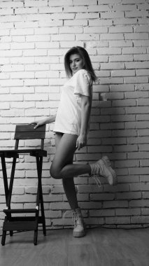 Stüdyoda sandalyenin yanında uzun saçlı, siyah beyaz bir kadın poz veriyor..  