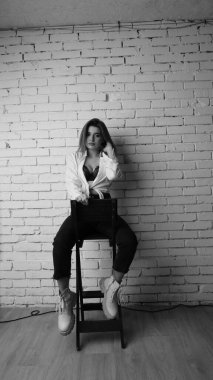 Beyaz tişörtlü, siyah beyaz saçlı, güzel ve seksi bir kadının stüdyoda beyaz bir duvara poz verdiği siyah beyaz bir fotoğraf..  