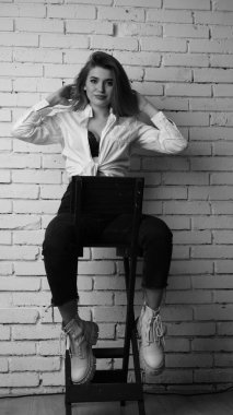 Beyaz tişörtlü, siyah beyaz saçlı, güzel ve seksi bir kadının stüdyoda beyaz bir duvara poz verdiği siyah beyaz bir fotoğraf..  