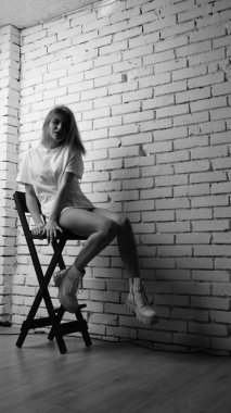 Stüdyoda sandalyenin yanında uzun saçlı, siyah beyaz bir kadın poz veriyor..  