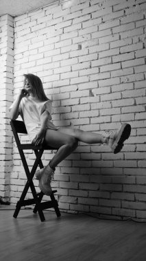 Stüdyoda sandalyenin yanında uzun saçlı, siyah beyaz bir kadın poz veriyor..  